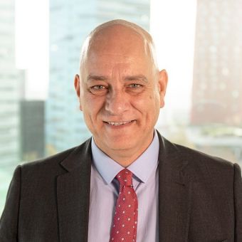 Smiling person wearing a suit and tie with city buildings in the background.