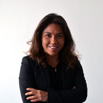 A person with long hair smiling, wearing a black suit against a white background.