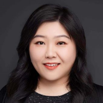 Smiling individual with dark hair against a gray background.