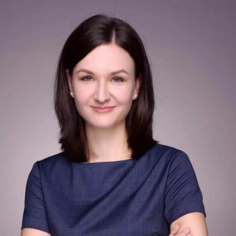 Person smiling with dark hair and blue top against gray background.