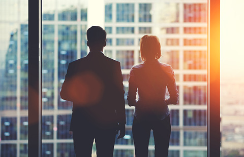 Silhouettes of two people looking out a window at a cityscape.