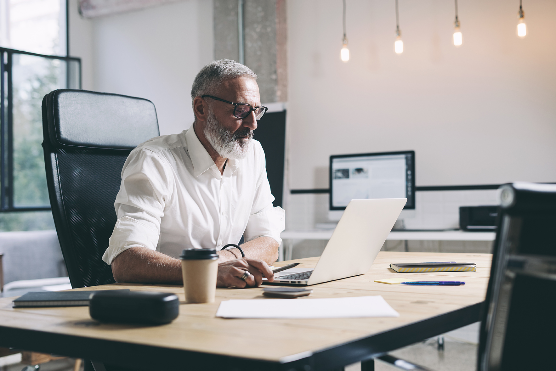Person working at a desk with a laptop and papers in a modern office setting.