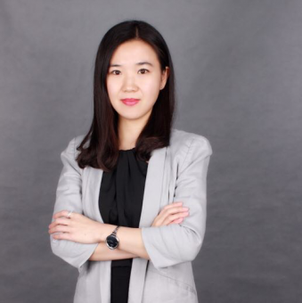 Person in a gray blazer with arms crossed, standing against a gray background.