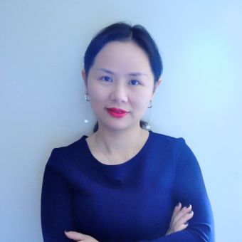 Person with crossed arms, wearing a dark blue top, standing against a light background.