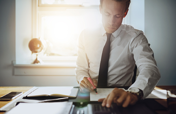 Person working at a desk with documents and a calculator in sunlight.