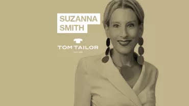 Person smiling, wearing a white blazer and large earrings, with text 'SUZANNA SMITH' and 'TOM TAILOR'.