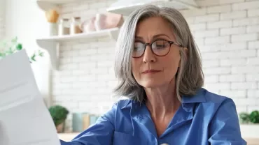Person in blue shirt reading a document in a bright kitchen.