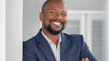 Person smiling in a suit, leaning against a pillar.