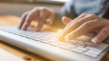 Close-up of hands typing on a white keyboard.