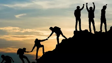 Silhouette of climbers helping each other on a mountain at sunset.