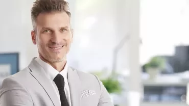 Smiling person in a light gray suit standing in a modern office.