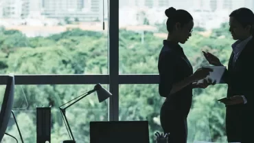 Two individuals discussing in an office with a window view of the city.