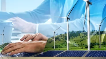 Hands typing on a laptop with wind turbines and solar panels in the background.