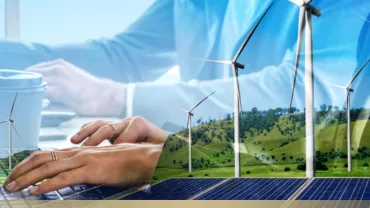 Hands typing on a laptop with wind turbines and solar panels in the background.