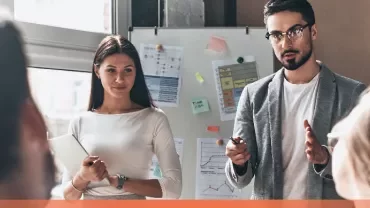 A team presenting in a modern office with charts on a whiteboard.
