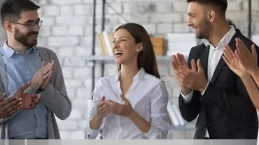 Group of colleagues in an office, smiling and clapping.