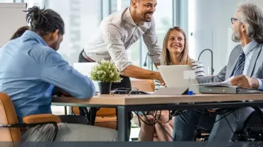 Smiling colleagues in a meeting room discussing around a table.