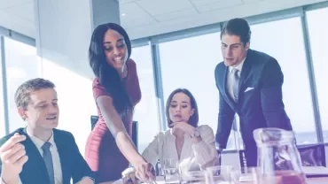 Group of colleagues discussing work around a table in a bright office.