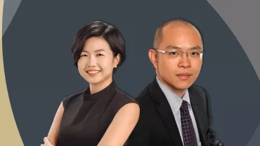 Two professionals smiling in formal attire against a geometric background.