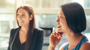 Two people smiling in a bright room.