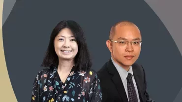 Two people smiling, one in a floral blouse and the other in a suit, against a geometric background.