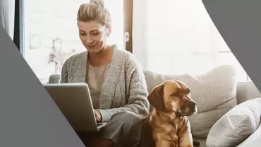 Person using a laptop on the couch with a dog beside them.