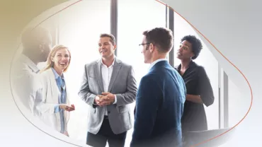Group of people in professional attire having a discussion by large windows.