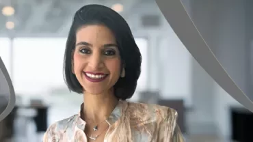 Person in patterned blouse standing in a modern office setting with curved graphic elements.