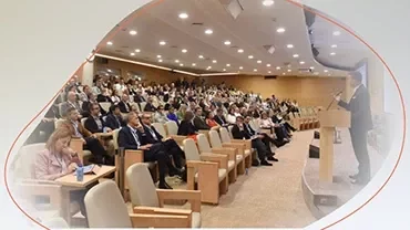 Large audience seated in an auditorium while a speaker presents at a podium.