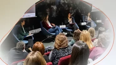 Panel discussion with several people seated on stage, speaking to an audience in a conference room.