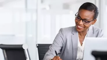 Professional working on a laptop and taking notes in an office setting.