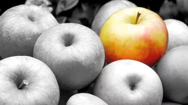 A single colored apple among grayscale apples.