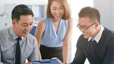 Three colleagues happily reviewing documents in an office setting.