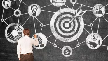 Person drawing a flowchart on a blackboard with target symbols and graphs.