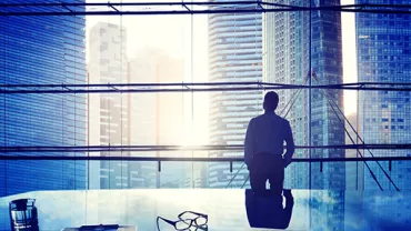 Person looking out at city skyline through large office window.
