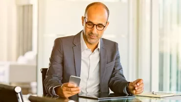 Person in a suit looking at their phone while sitting at a desk.