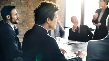 People in a meeting room with a brick wall and sunlight streaming through windows.