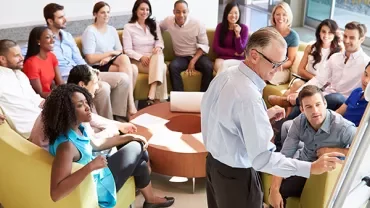 A group of people in a relaxed meeting setting with a speaker at the front.