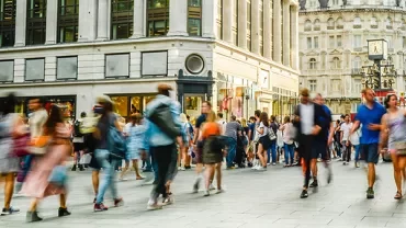 A bustling city street with people walking past shops.