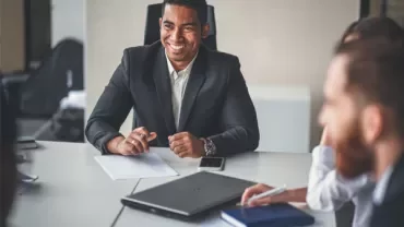 Person in a suit smiling during a meeting at a conference table.