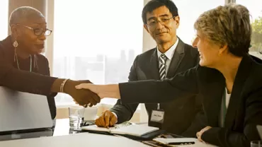 Three people in a meeting room, two shaking hands and smiling.