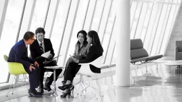 Group of four people seated in a modern office, engaged in discussion.