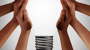 Diverse hands surround a coiled bulb base, symbolizing teamwork and innovation.
