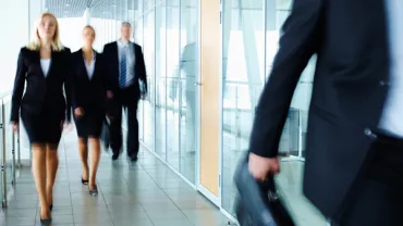 People in business attire walking in a modern office hallway.