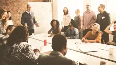 A diverse team having a discussion around a whiteboard in a bright meeting room.