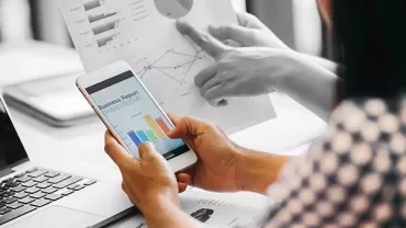 Person holding a smartphone displaying a business report with colorful charts.