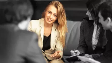 Person in a suit leading a group discussion, seated in a professional setting.