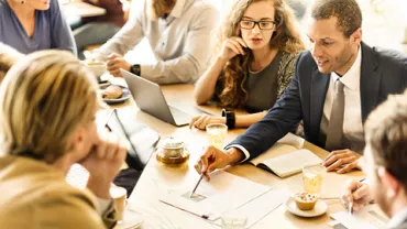 Group of people discussing in a meeting with laptops and notebooks on a table.