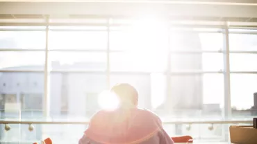 Person sitting at a table with sunlight streaming through a large window.