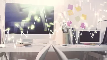 Office with computers displaying graphs, white desks, and colorful sticky notes.